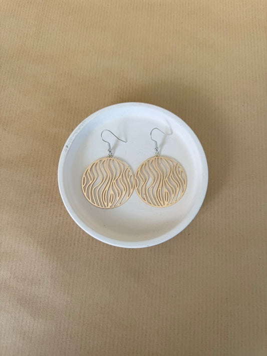 Gold earrings on a white dish against a beige background
