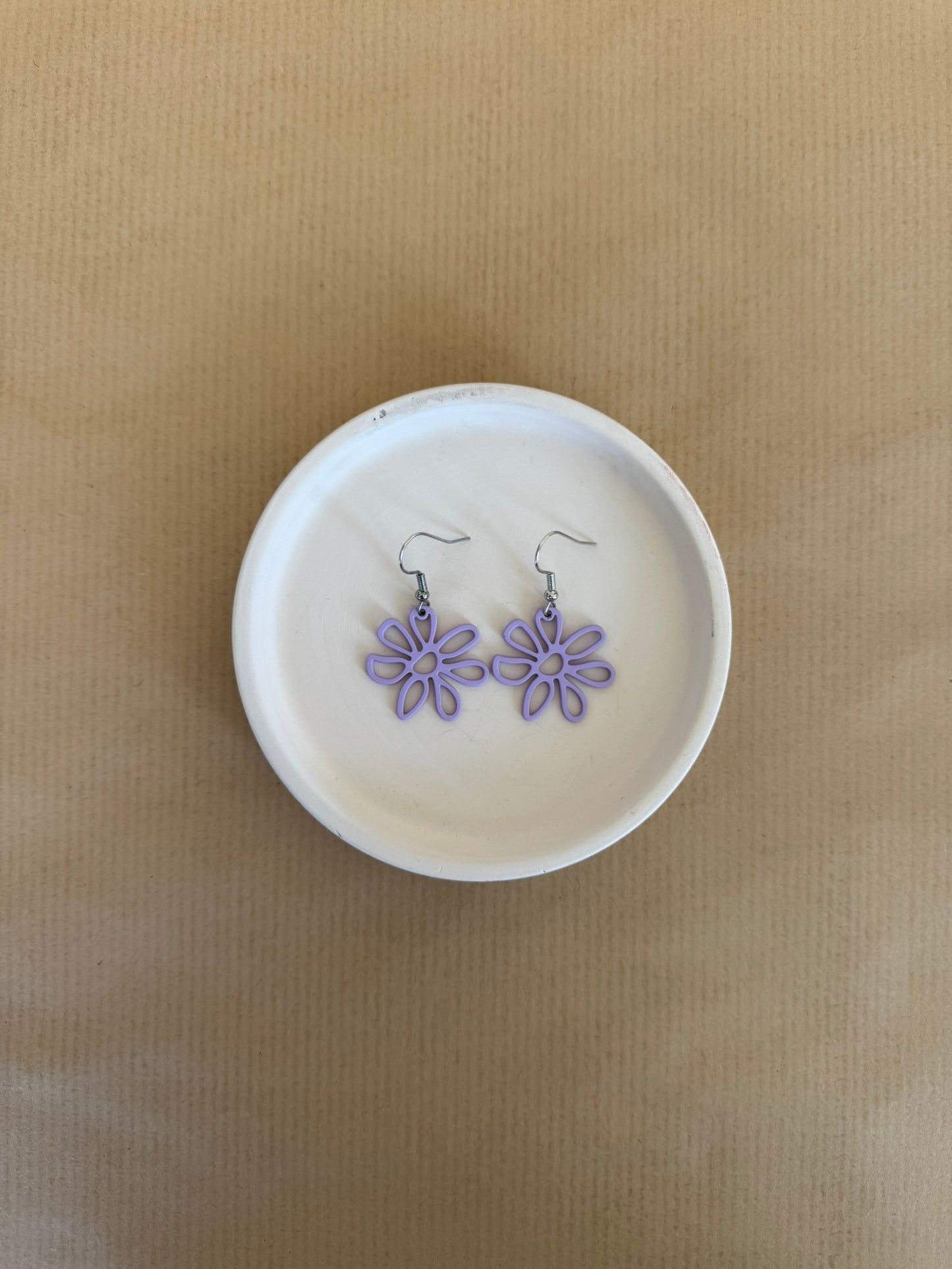 Purple Flower-shaped earrings on a white dish against a brown background