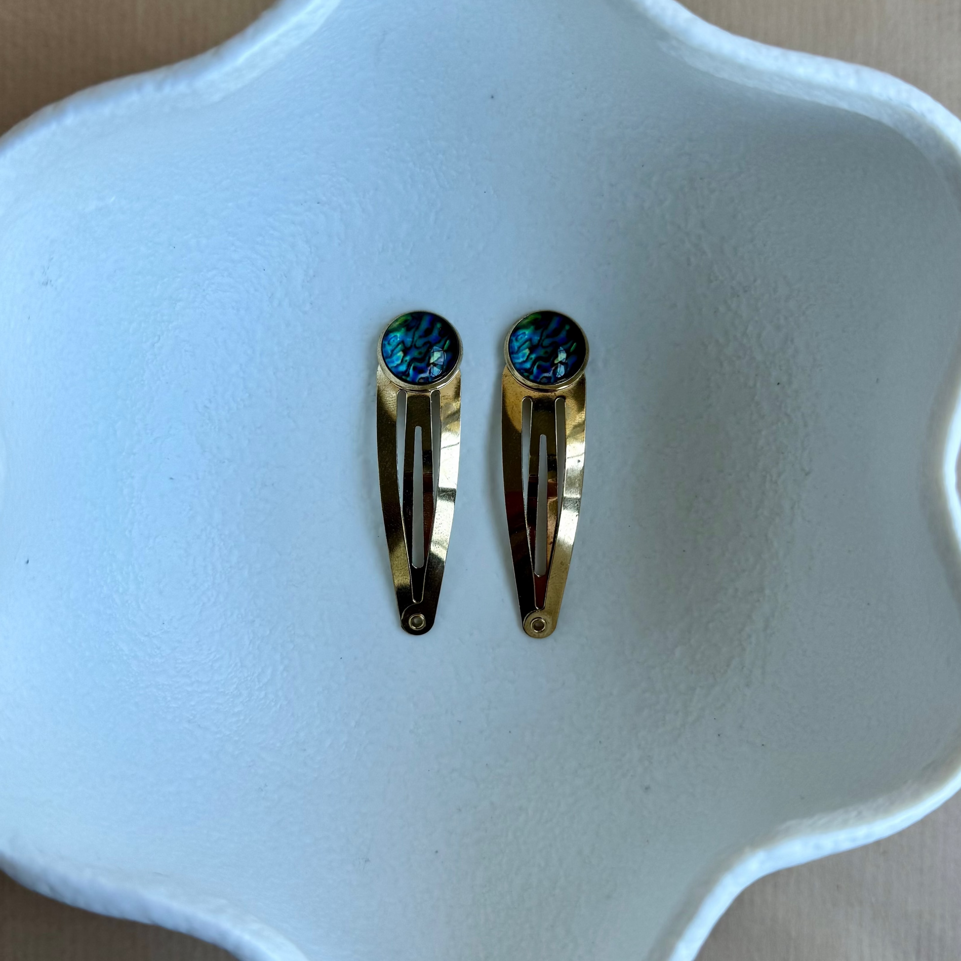 Gold hair clips with blue gemstones on a white dish