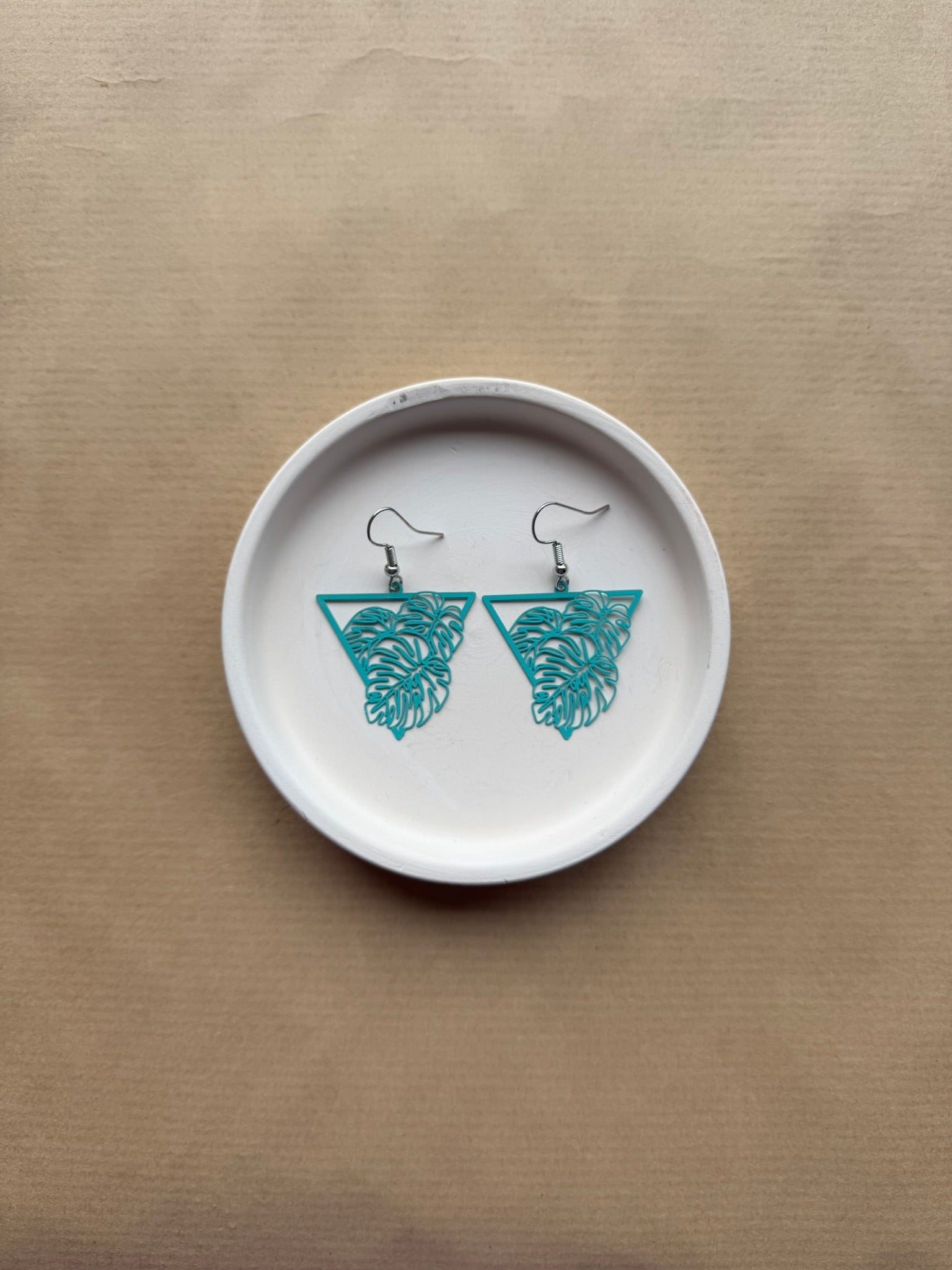White ceramic dish with blue leaf earrings on a beige background
