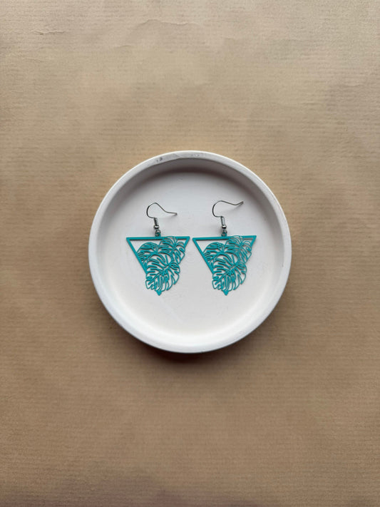 White ceramic dish with blue leaf earrings on a beige background