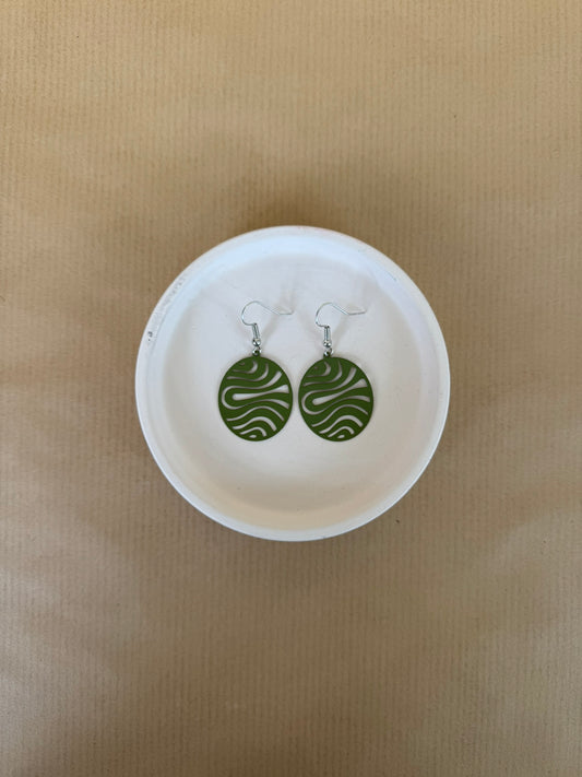 Green circular earrings on a white dish against a beige background