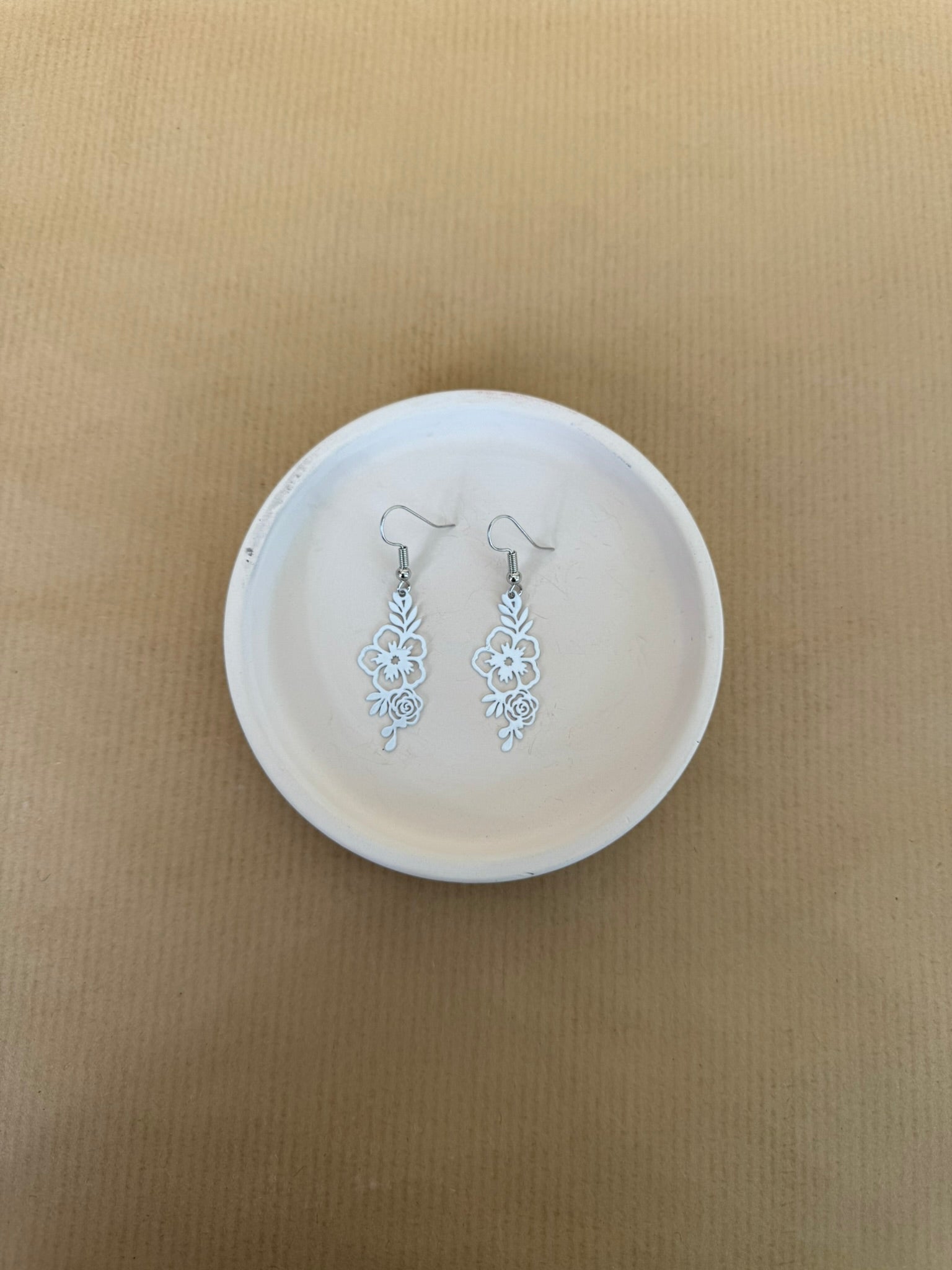 white Floral earrings on a white dish against a beige background