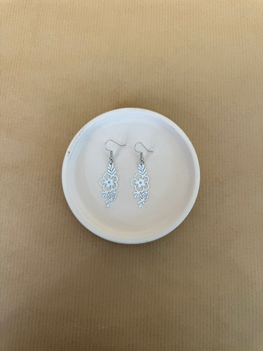 white Floral earrings on a white dish against a beige background