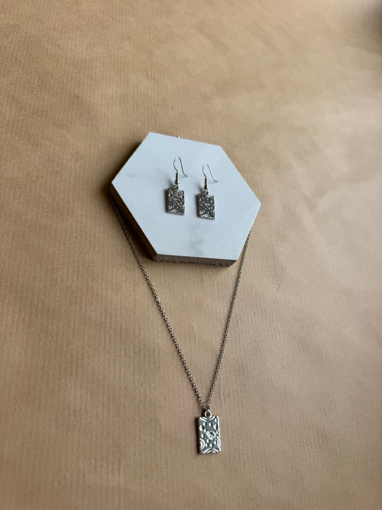 Silver necklace and earrings on a hexagonal white stand with a beige background
