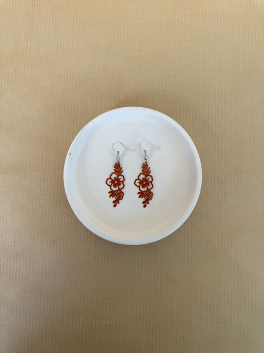 burnt orange earrings on a white circular stand against a beige background