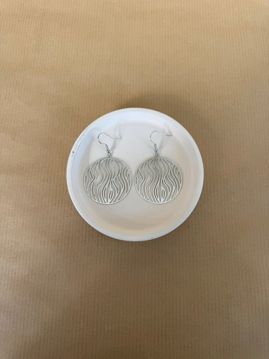 Silver earrings on a white circular stand against a beige background