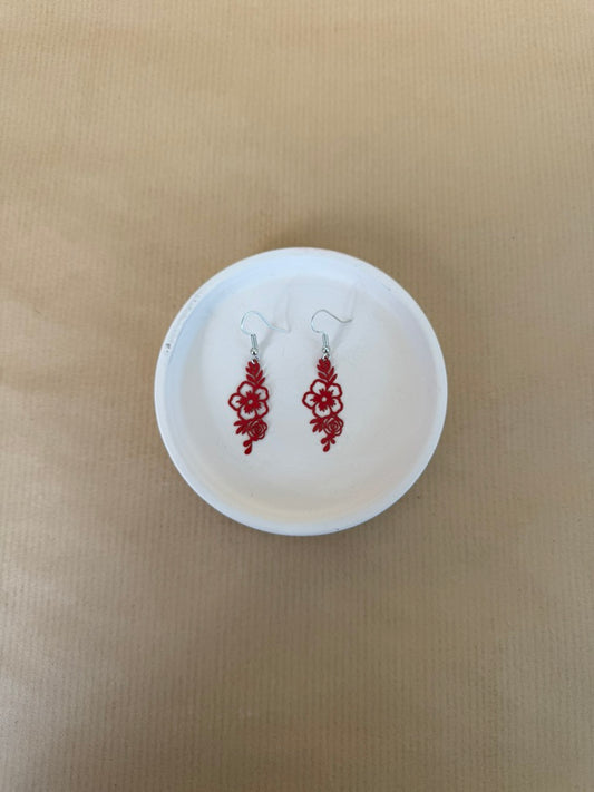Red earrings on a white circular stand against a beige background
