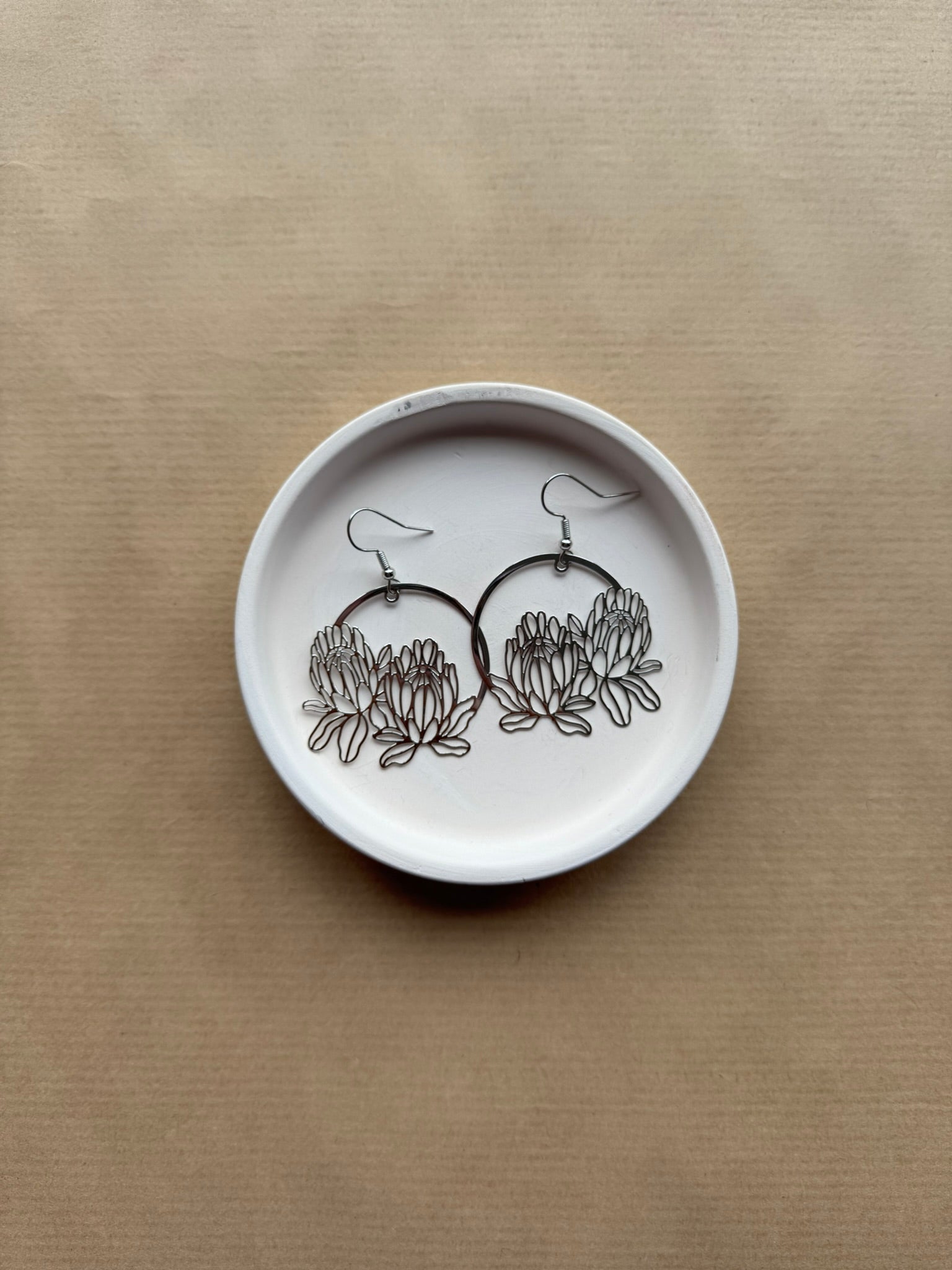 White dish with floral earrings on a beige background