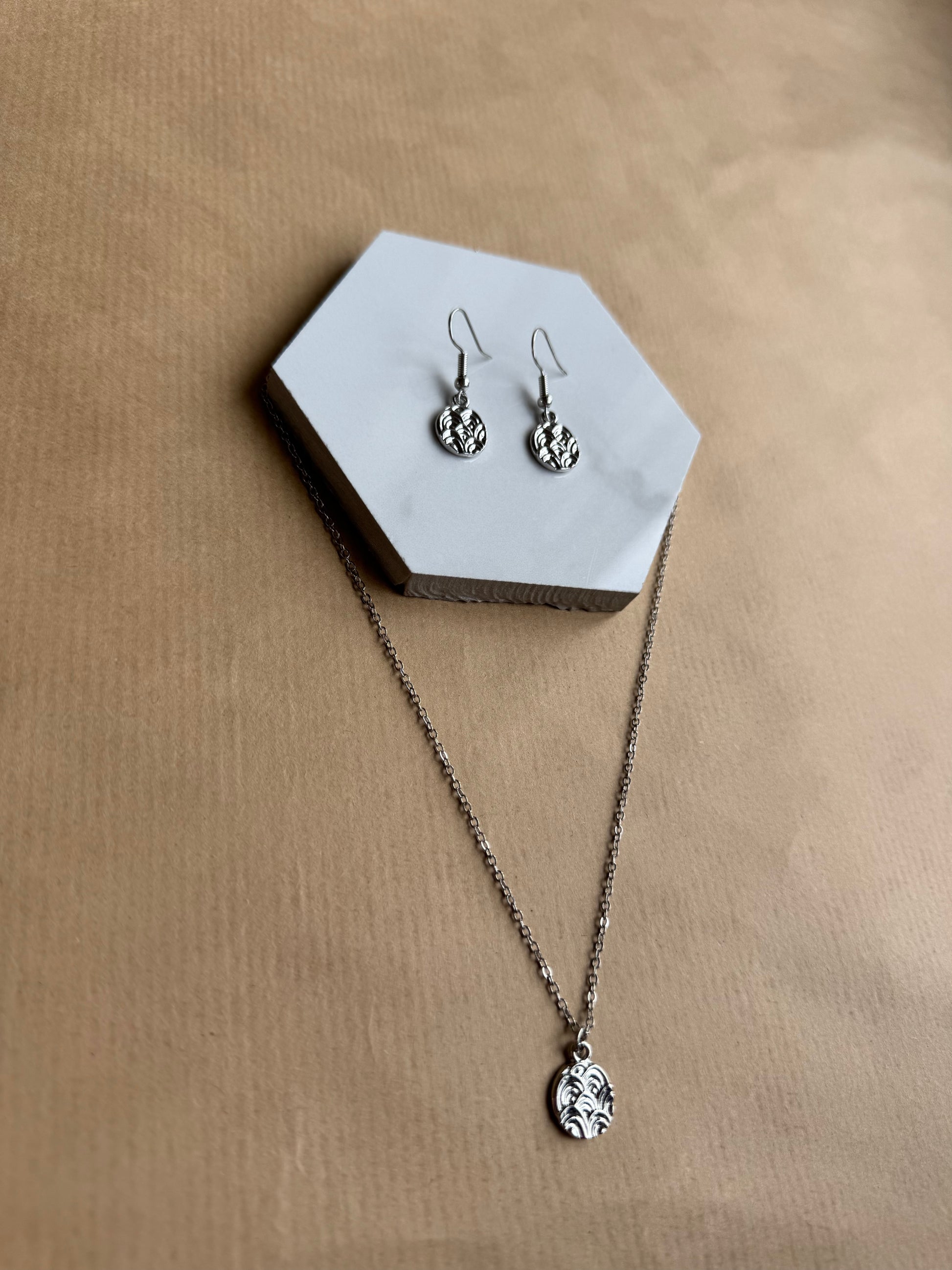 Silver necklace and earrings on a hexagonal white stand against a beige background