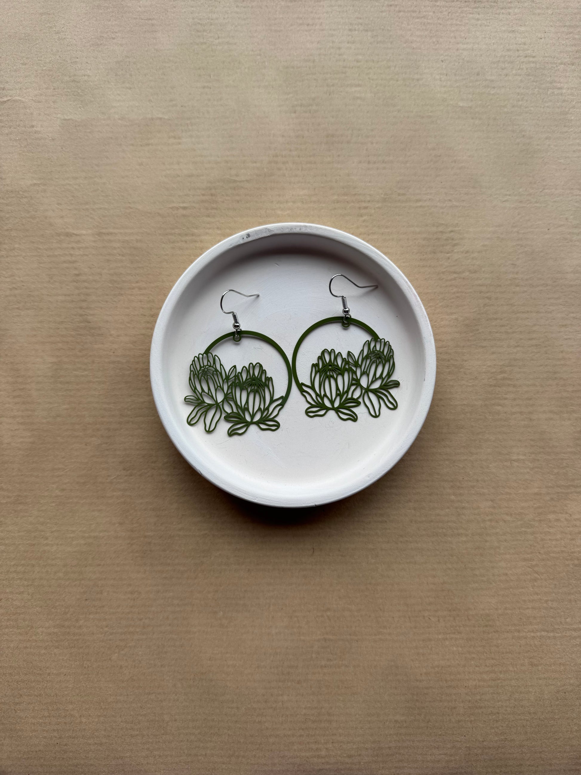 White dish with green floral earrings on a beige background