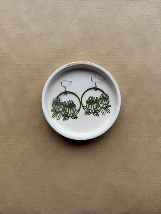 White dish with green floral earrings on a beige background