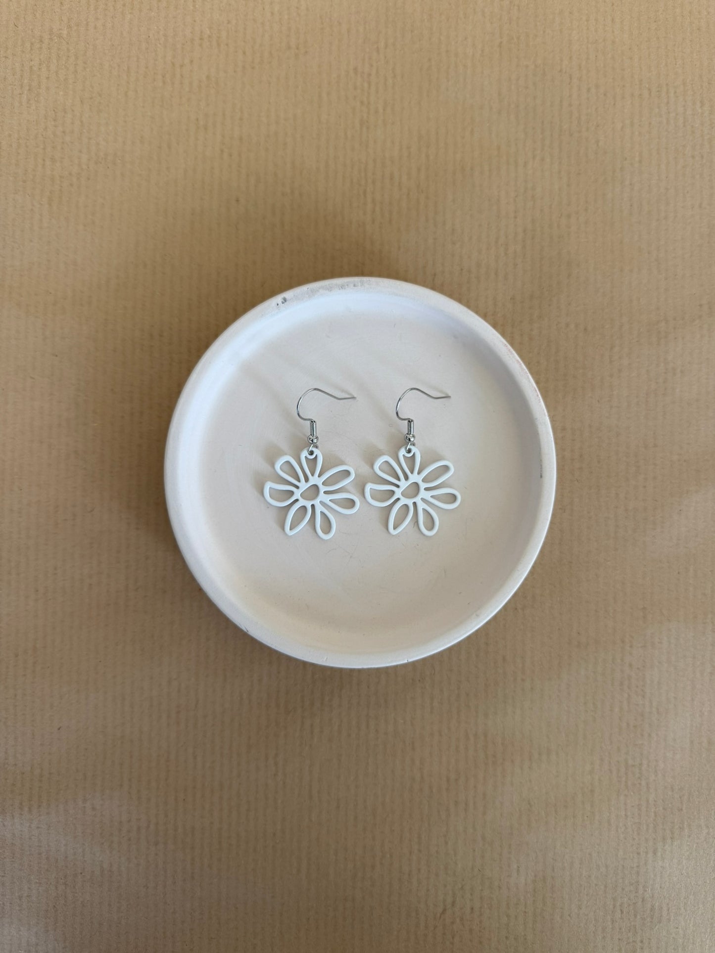 White flower-shaped earrings on a beige background