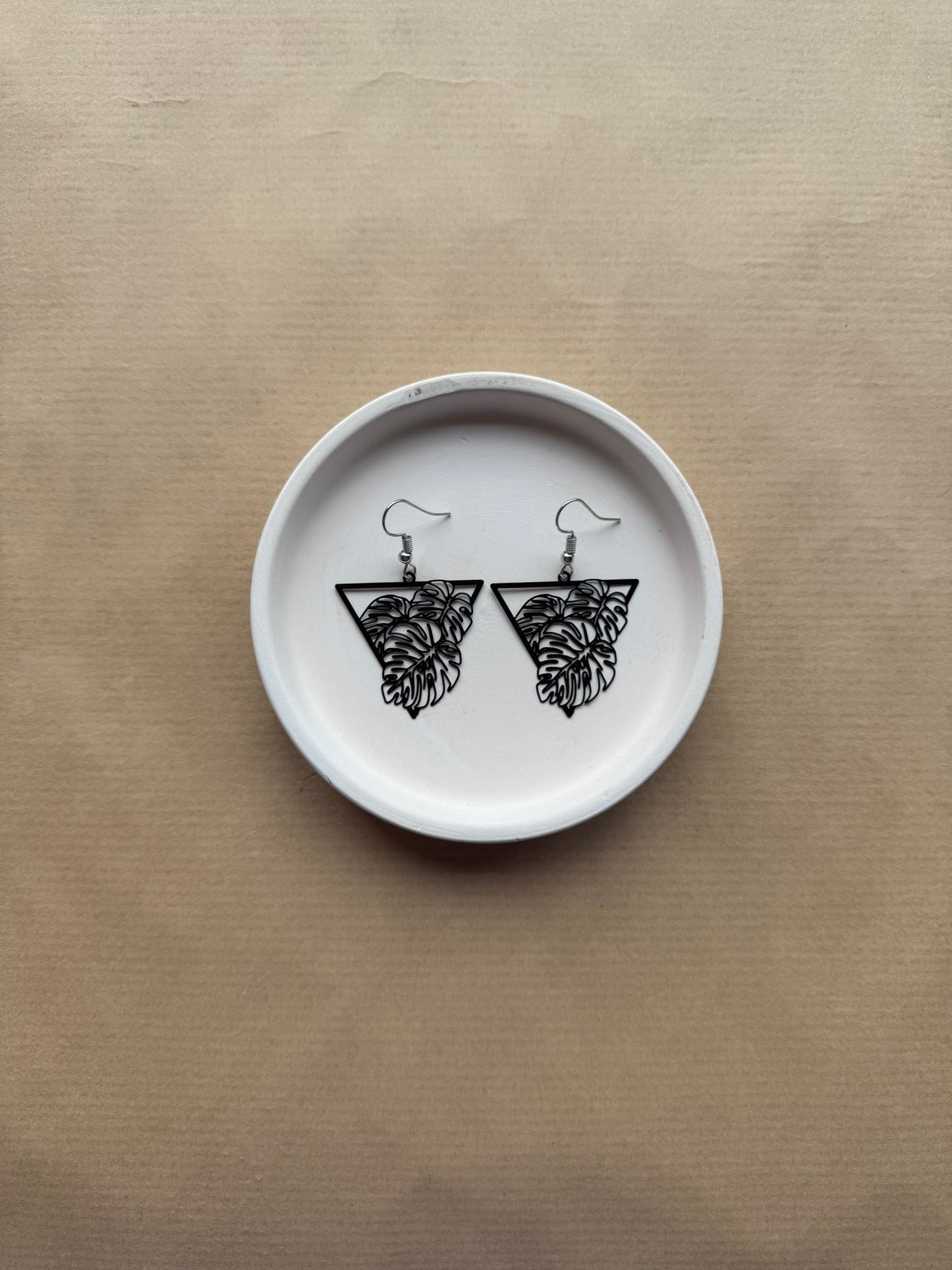 White ceramic plate with black leaf earrings on a beige background