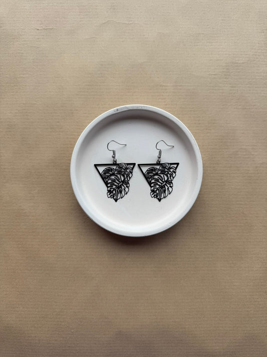 White ceramic plate with black leaf earrings on a beige background