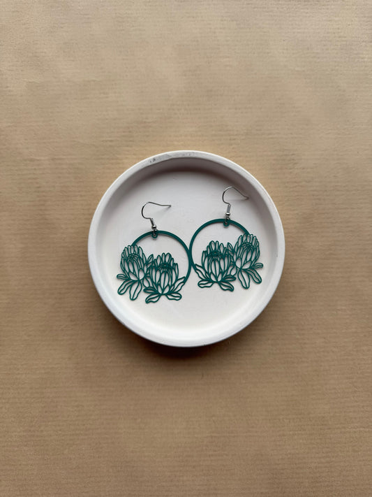 Pair of earrings with floral design on a white dish against a beige background