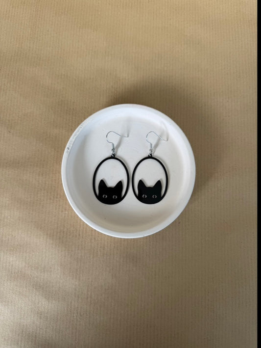 Cat-shaped earrings in a white round container on a beige surface