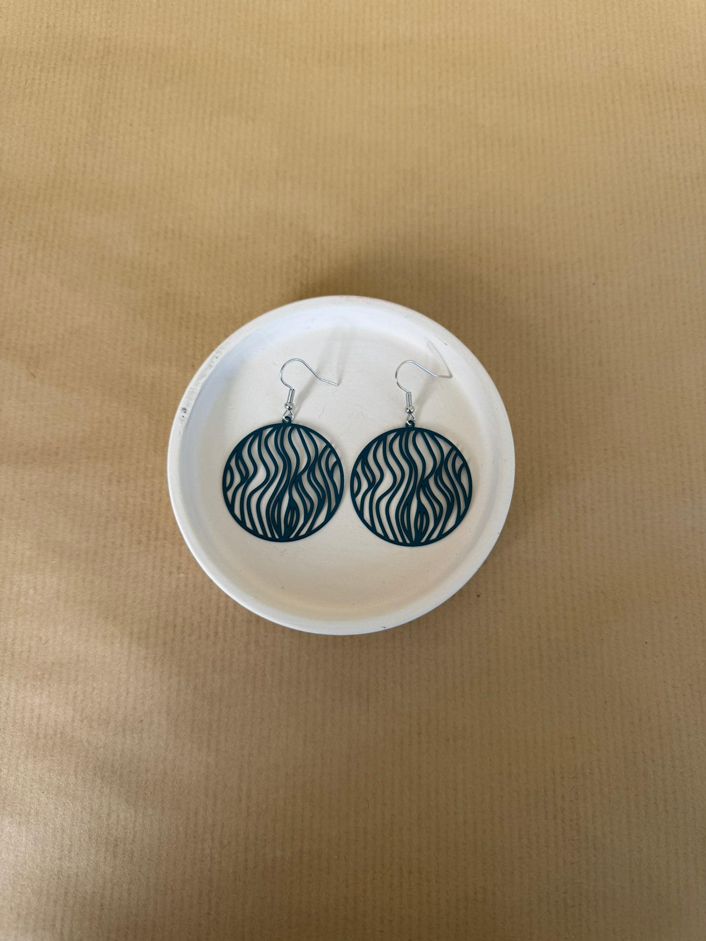 Teal Pair of earrings on a white circular stand against a beige background