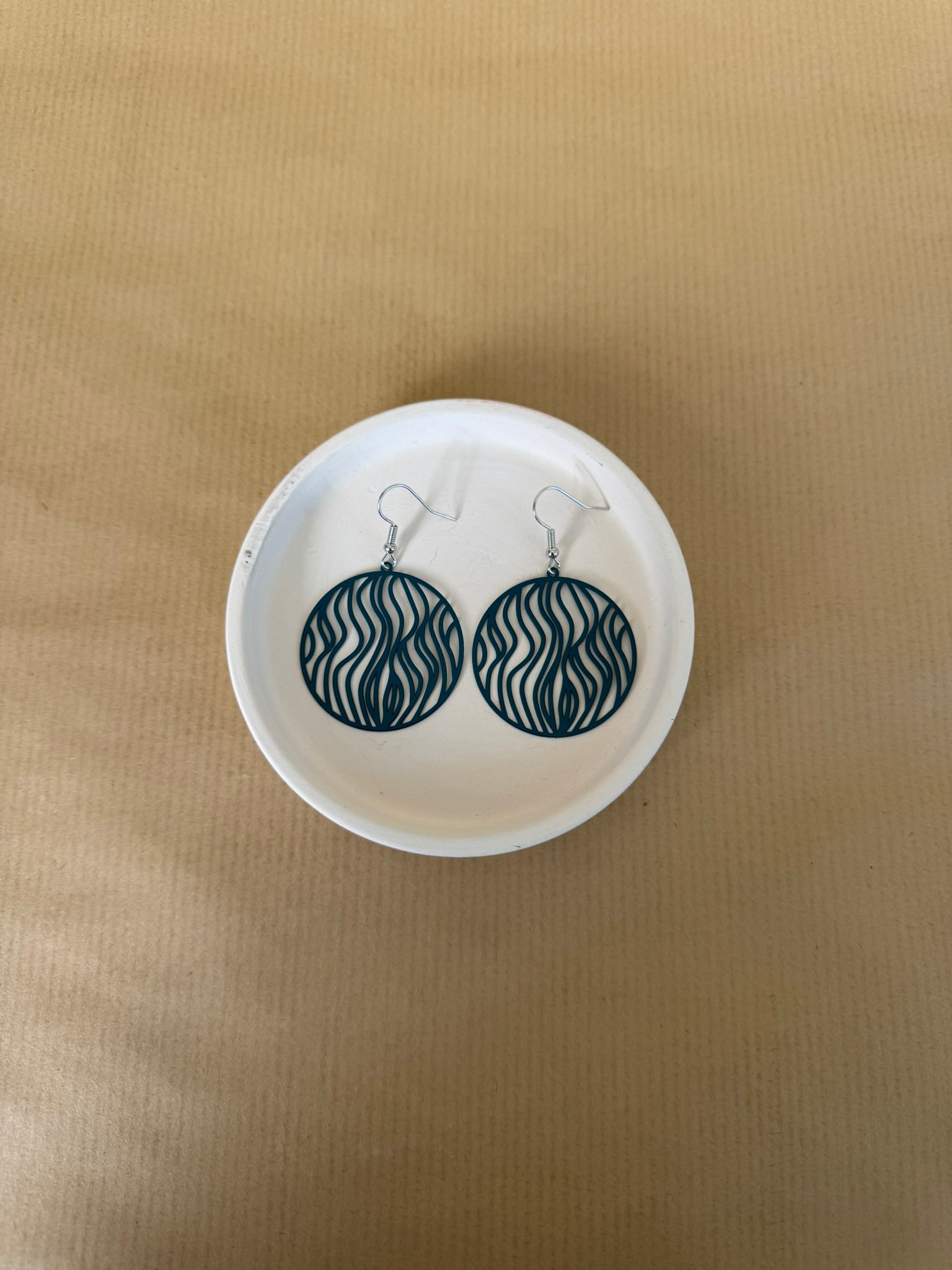 Teal Pair of earrings on a white circular stand against a beige background