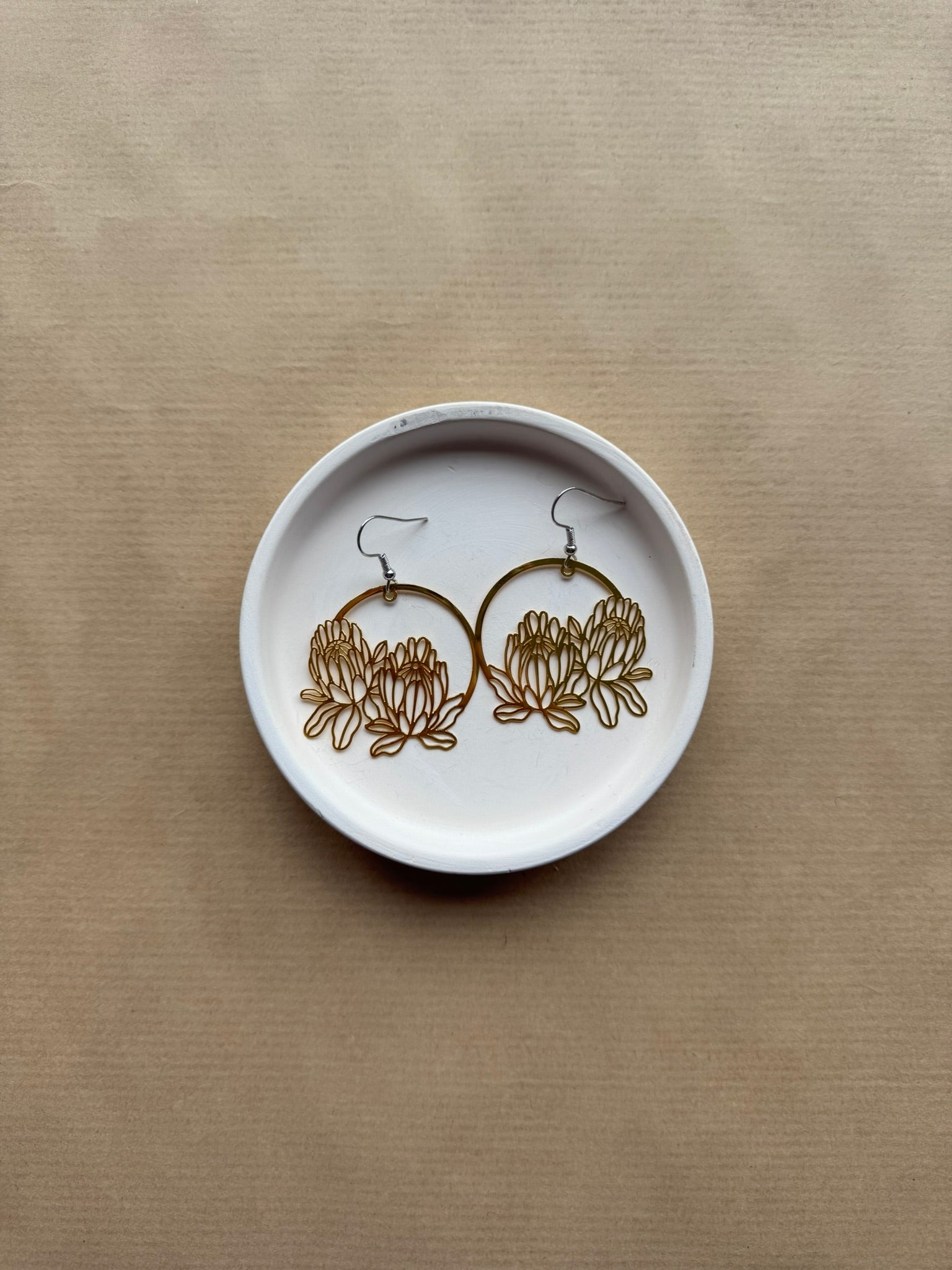 Pair of gold earrings on a white dish against a beige background