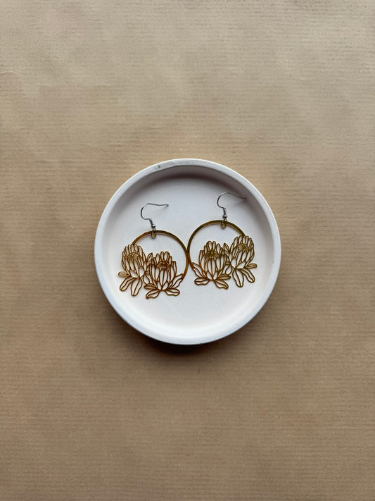 Pair of gold earrings on a white dish against a beige background