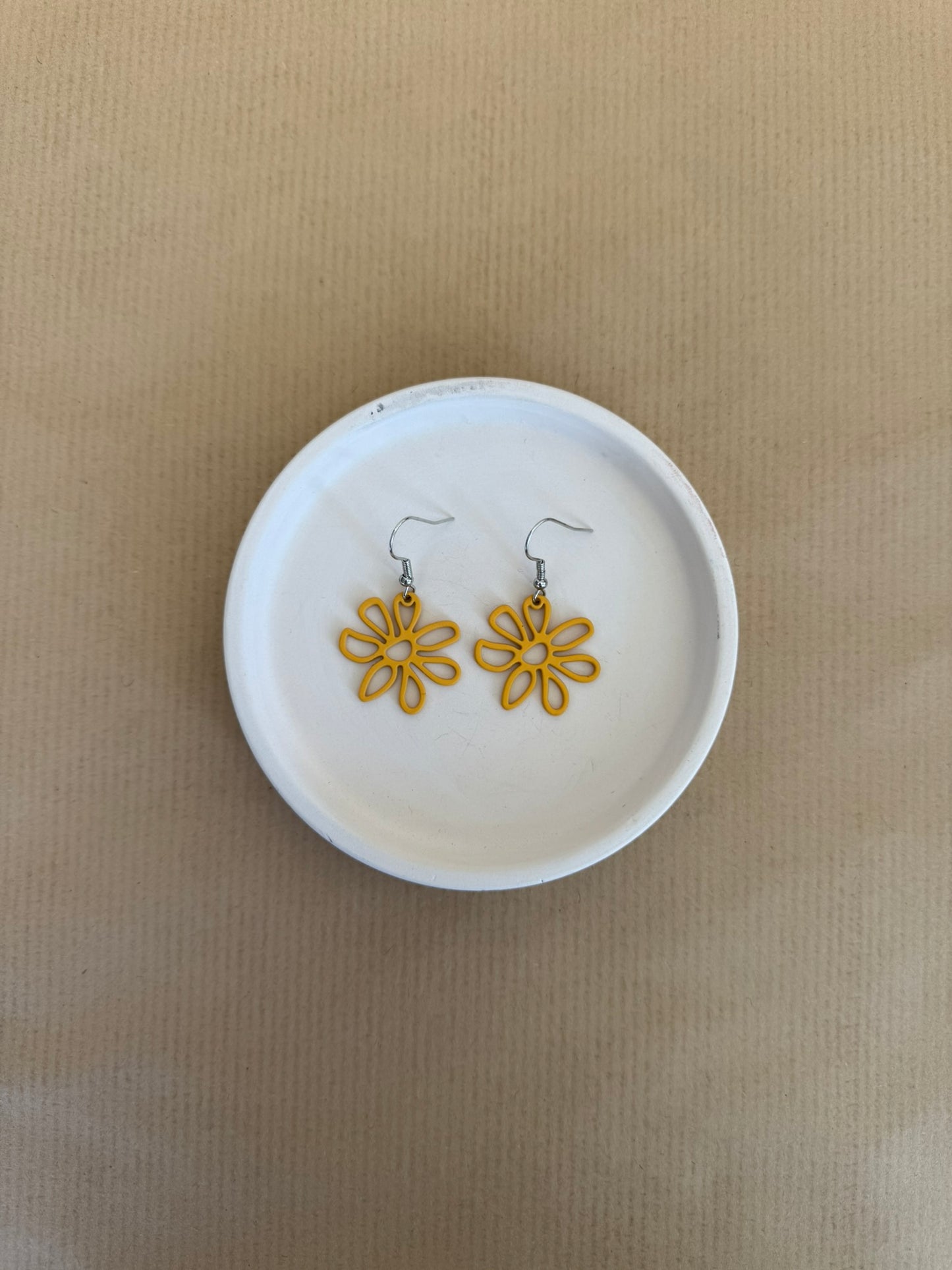 Mustard flower-shaped earrings on a white dish against a beige background