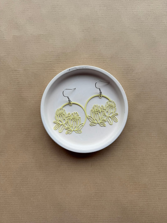 Yellow earrings on a white dish against a beige background