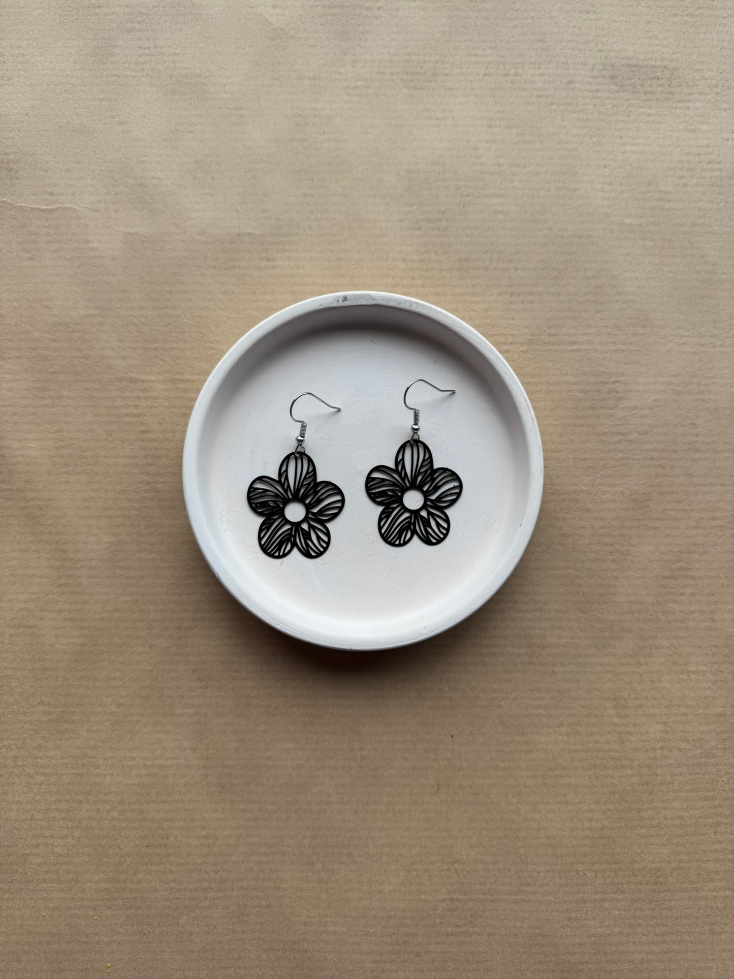 Flower-shaped earrings on a white dish against a beige background