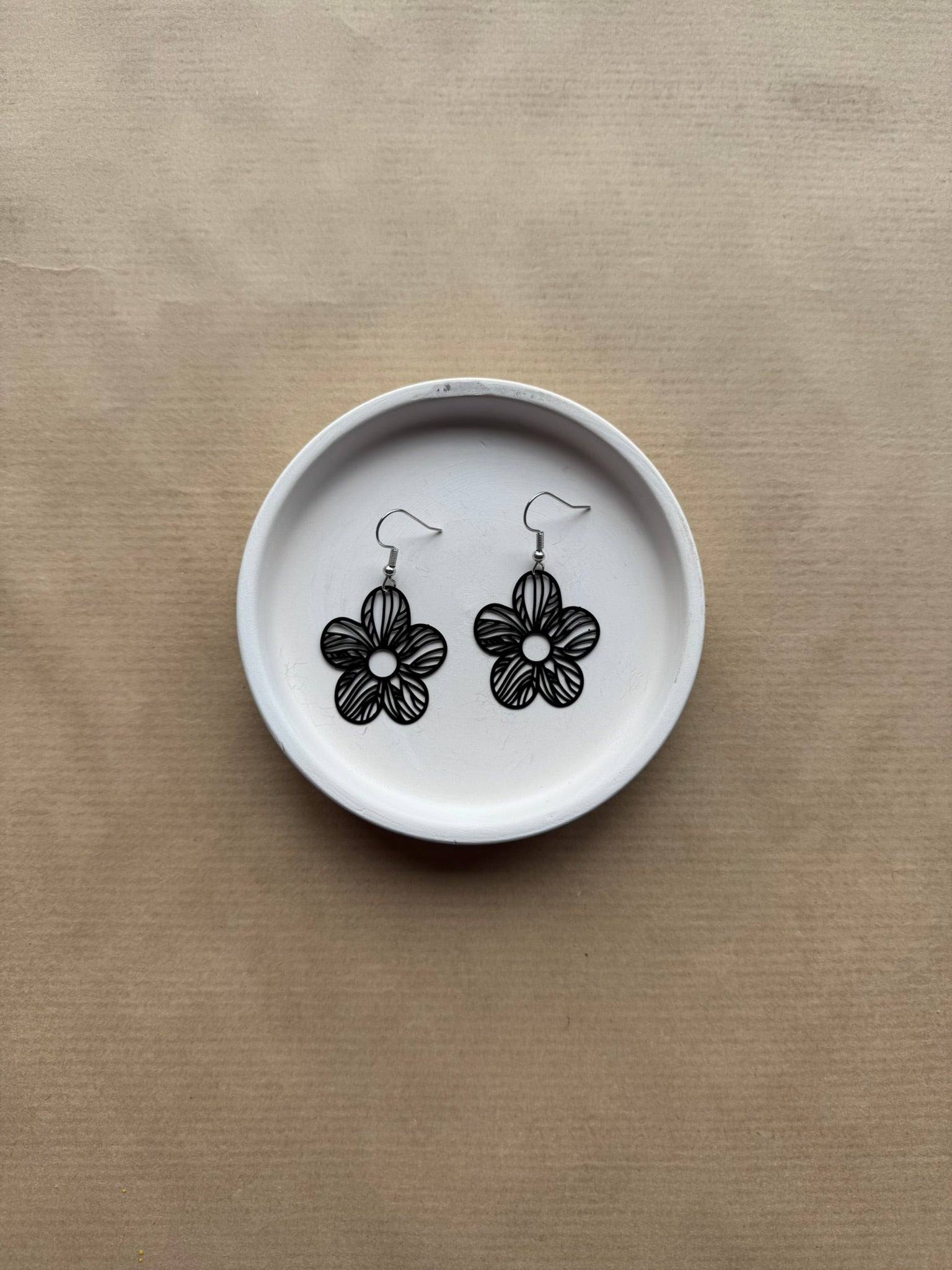 Flower-shaped earrings on a white dish against a beige background