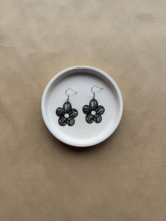 Flower-shaped earrings on a white dish against a beige background