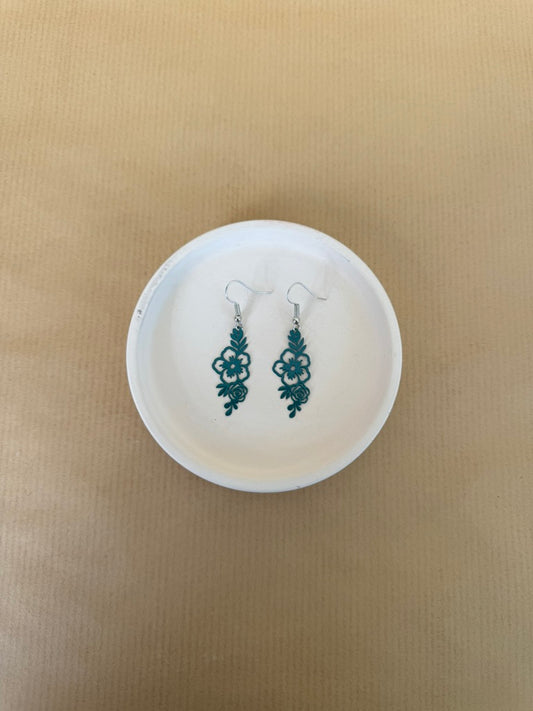 Pair of teal earrings on a white dish against a beige background