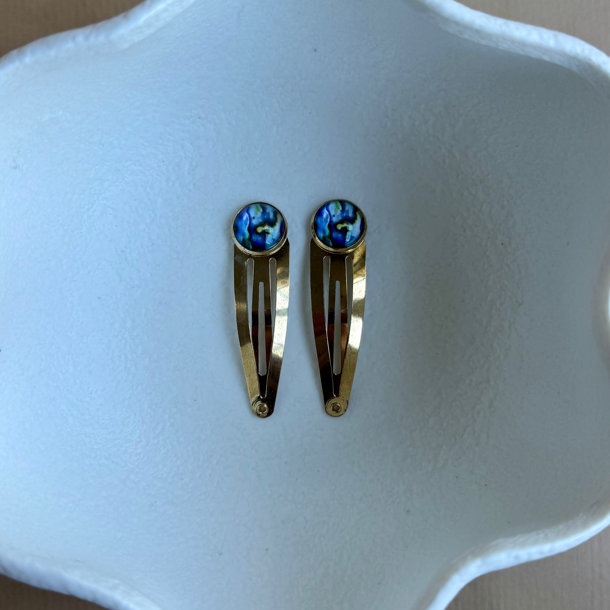 Gold hair clips with blue gemstones on a white dish
