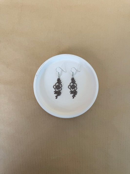 Pair of brown floral earrings on a white round stand against a beige background
