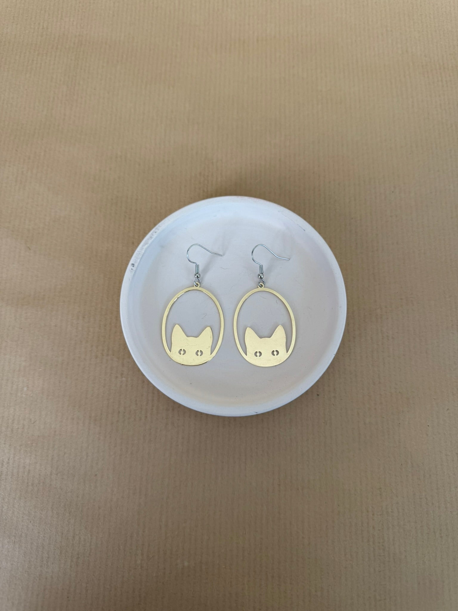 Gold cat-shaped earrings on a white circular stand against a beige background