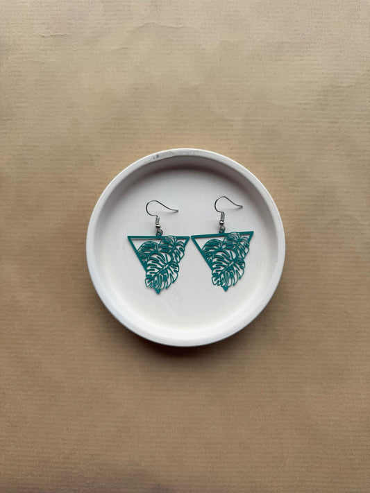 Teal leaf-shaped earrings on a white dish against a beige background