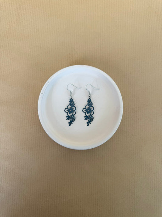 Dark blue earrings on a white circular stand against a beige background