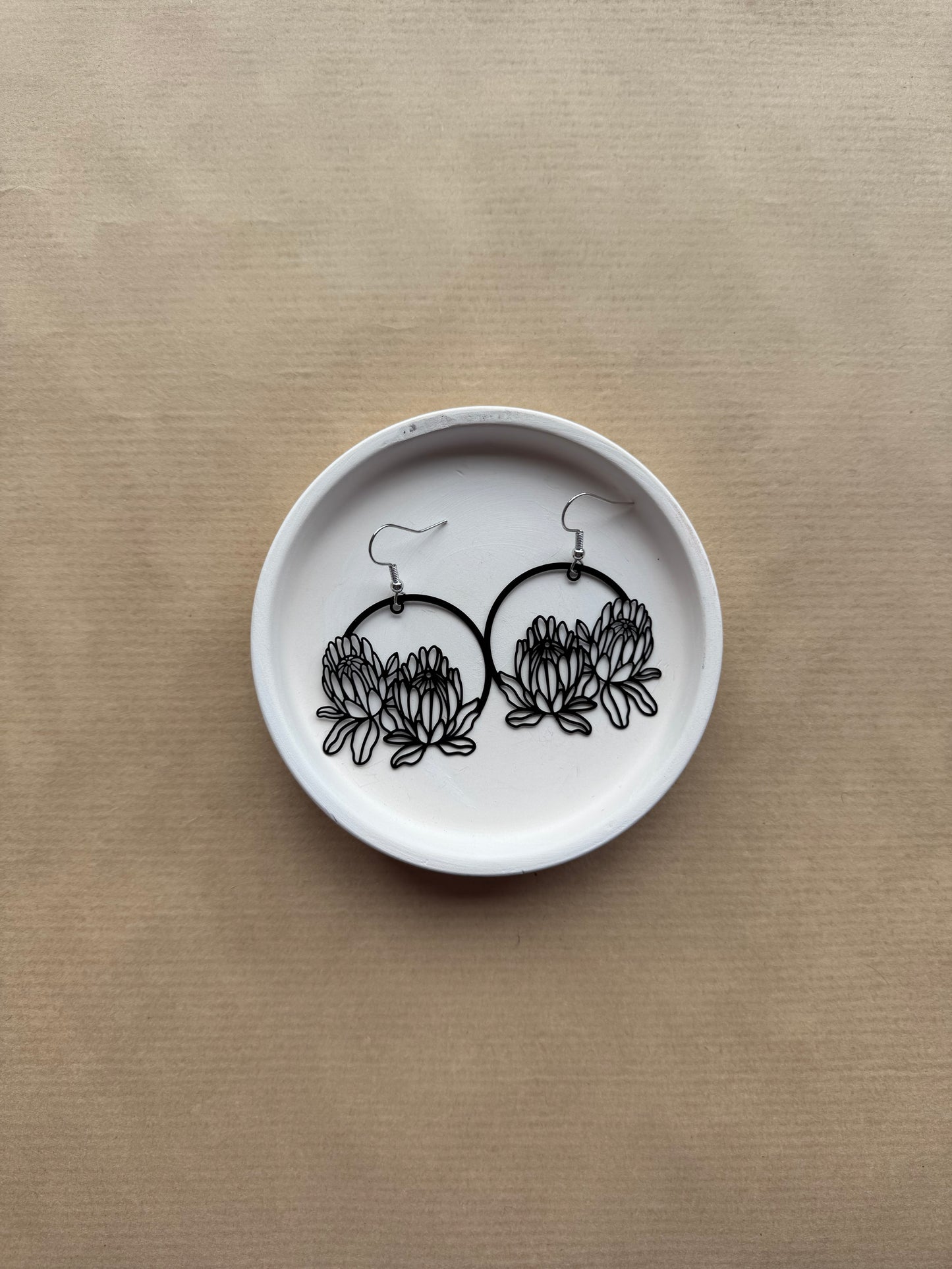 White dish with black floral earrings on a beige background