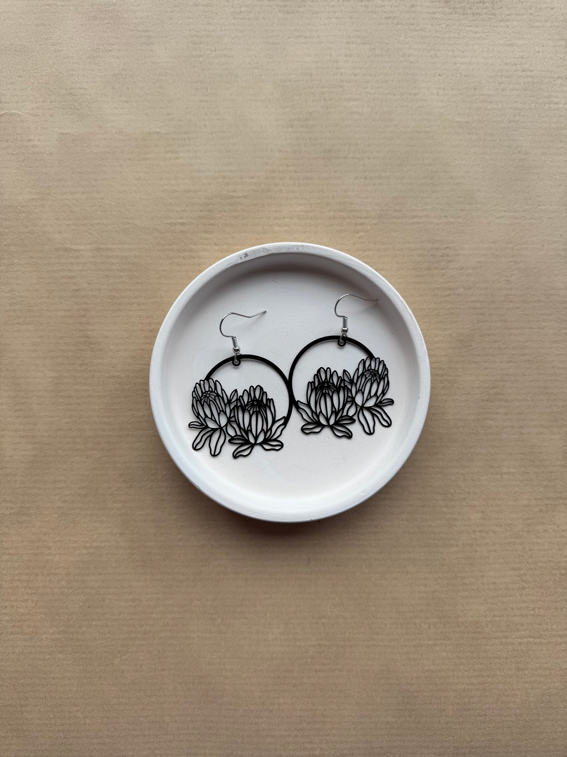 White dish with black floral earrings on a beige background