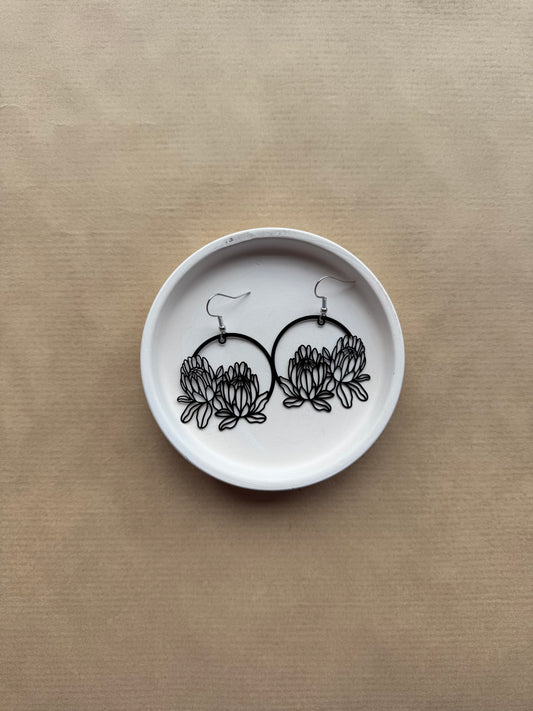White dish with black floral earrings on a beige background