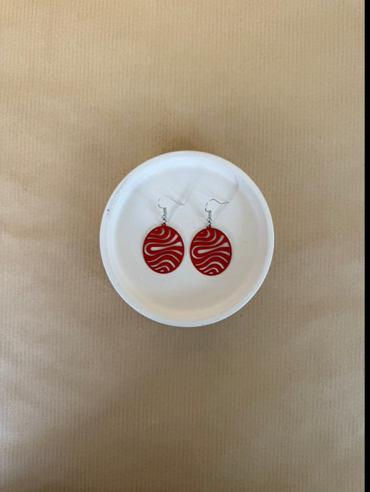 Pair of red earrings on a white dish against a beige background