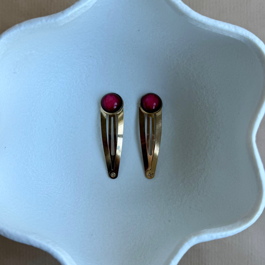 Two gold hair clips with red stones on a white ceramic dish.
