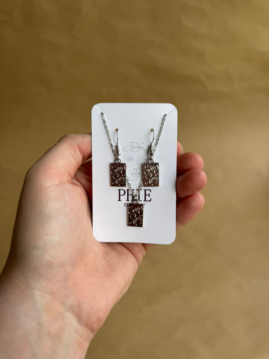 Hand holding a necklace set on a branded card against a brown background